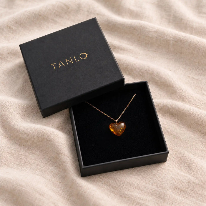 Klasikinio gintaro širdelės pakabukas „Širdelė“ ant paauksuotos grandinėlės juodoje „Tanlo“ dovanų dėžutėje, ant lininio audinio.